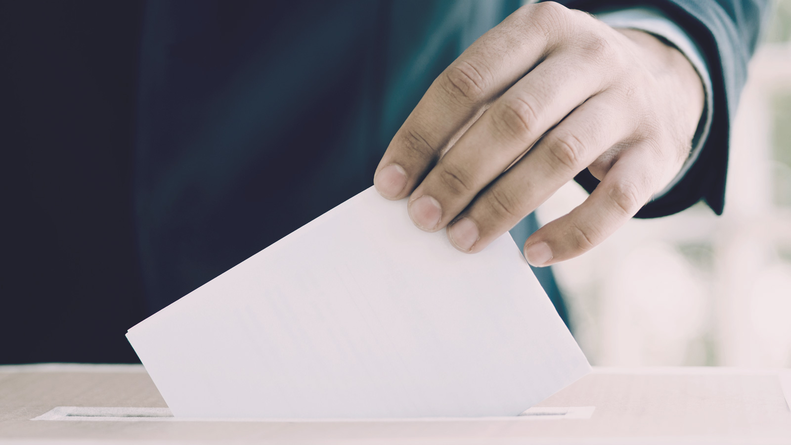 A hand posting a voting slip into a ballot box