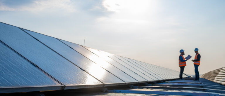 Two men stand on a roof between rows of net zero photovoltaic panels