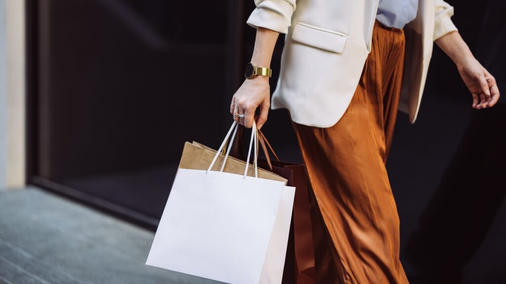 Woman carrying paper shopping bags walking on a city pavement.