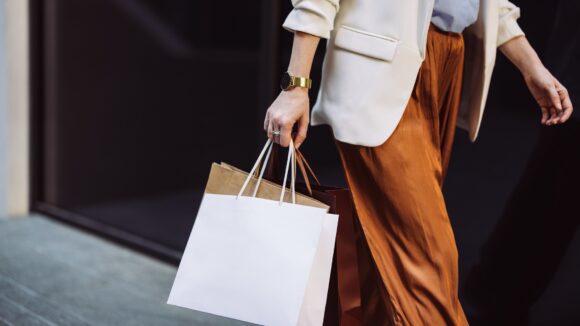 Woman carrying paper shopping bags walking on a city pavement.