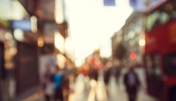Blurred photo of shoppers walking down a high street in London with a bus in view.