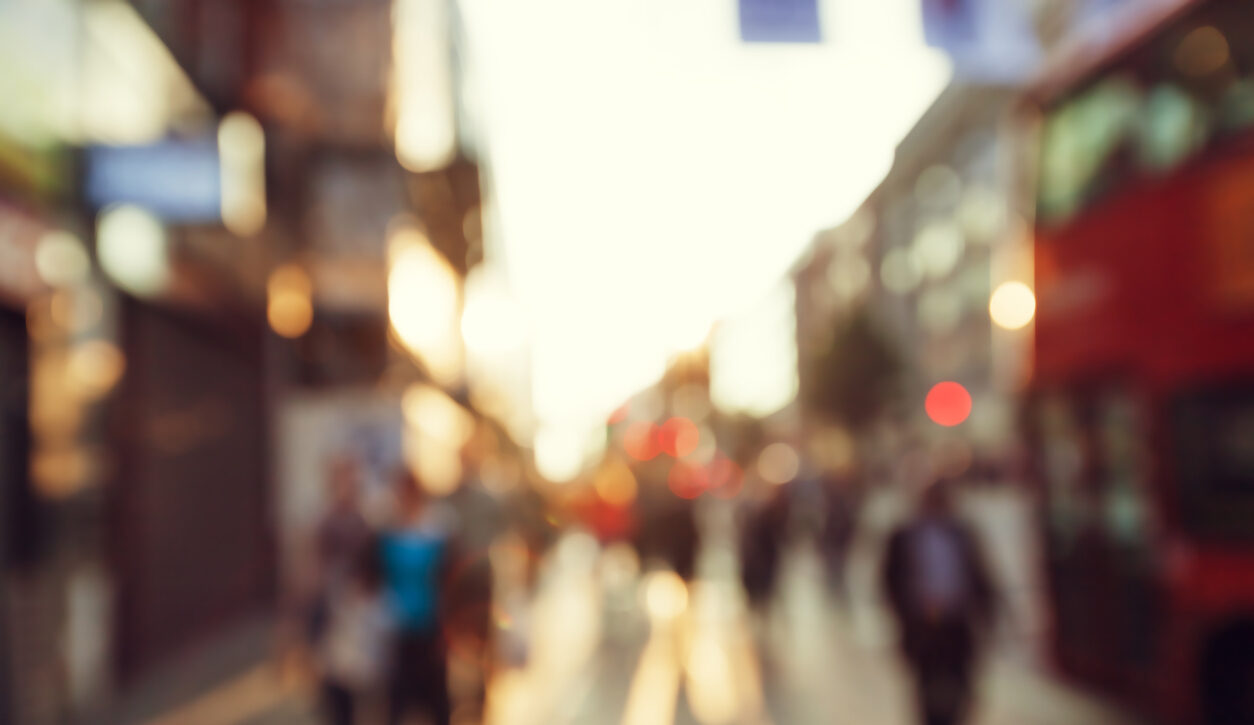 Blurred photo of shoppers walking down a high street in London with a bus in view.