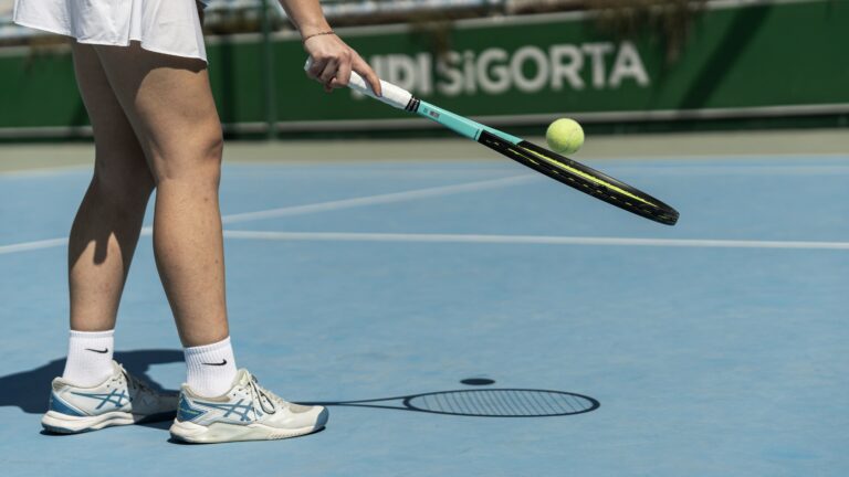 Female tennis player lifting up the ball with the racket