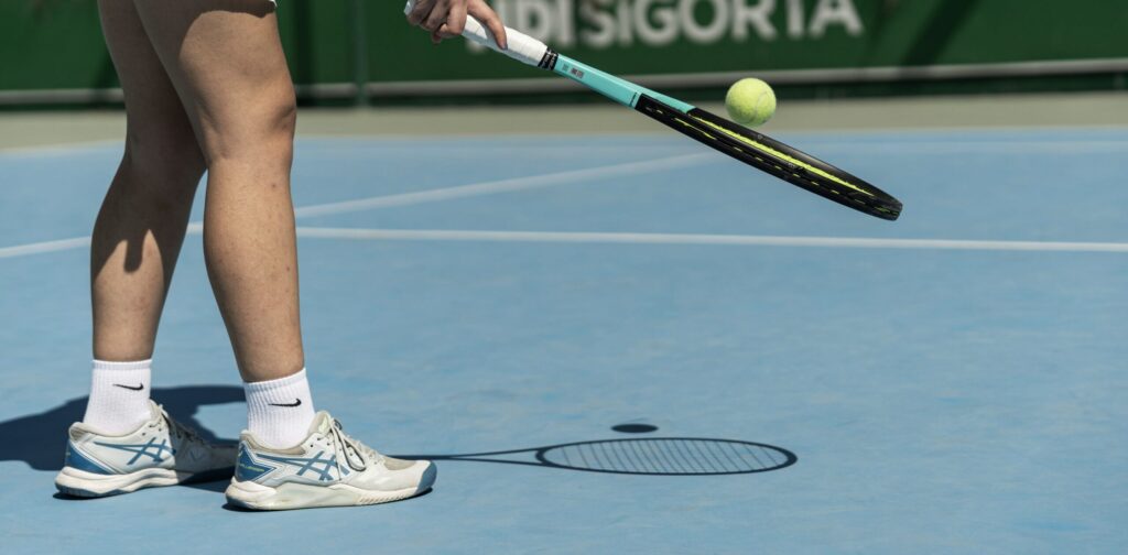 Female tennis player lifting up the ball with the racket