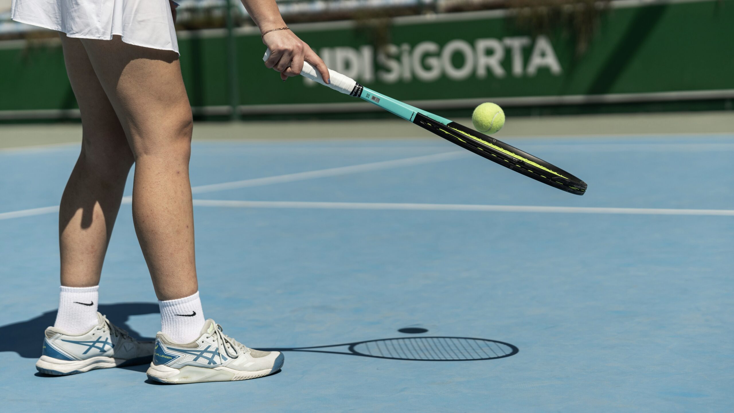 Female tennis player lifting up the ball with the racket