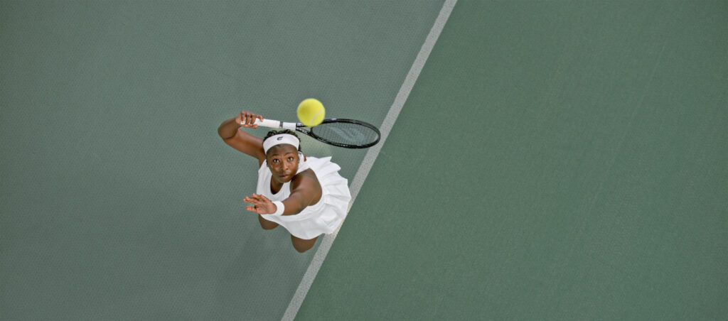 Woman photographed mid-serve while playing tennis